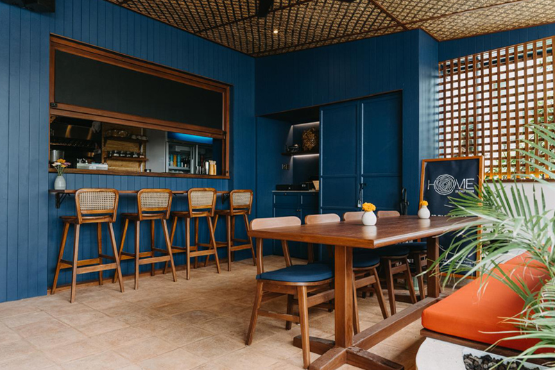 At HOME by Chef Wayan, recently revamped, showcasing a stylish dining area with a vibrant blue wall and a cozy bar.